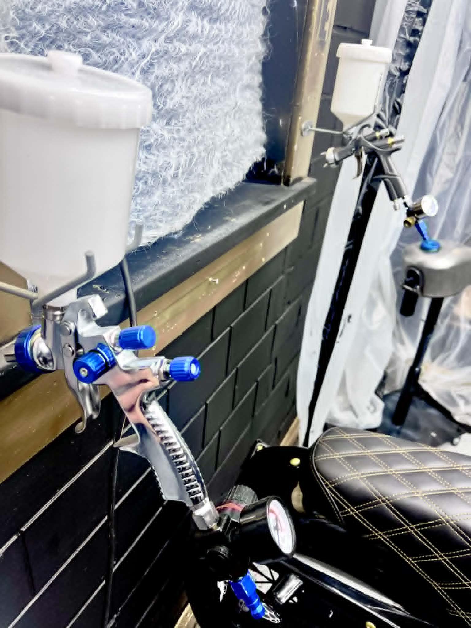 HVLP spray guns racked at the booth — blue paint cups, pressure gauge