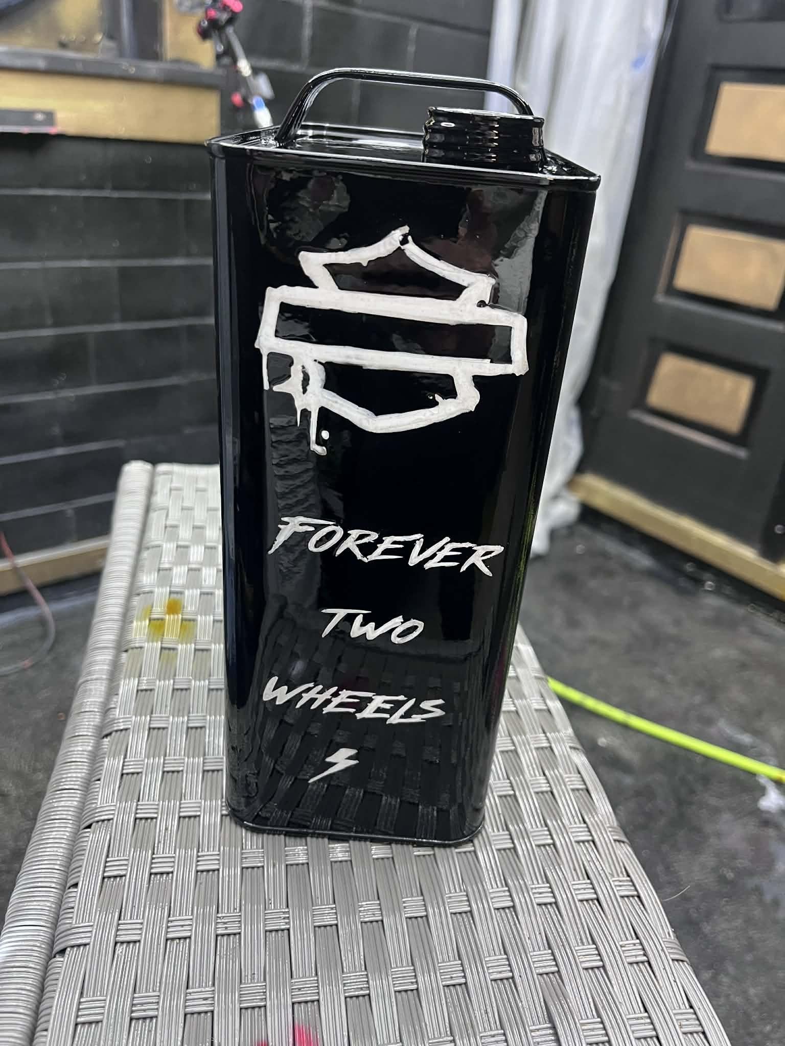 Gloss-black Harley-Davidson tank with gold "Forever Two Wheels" script, staged on the booth floor